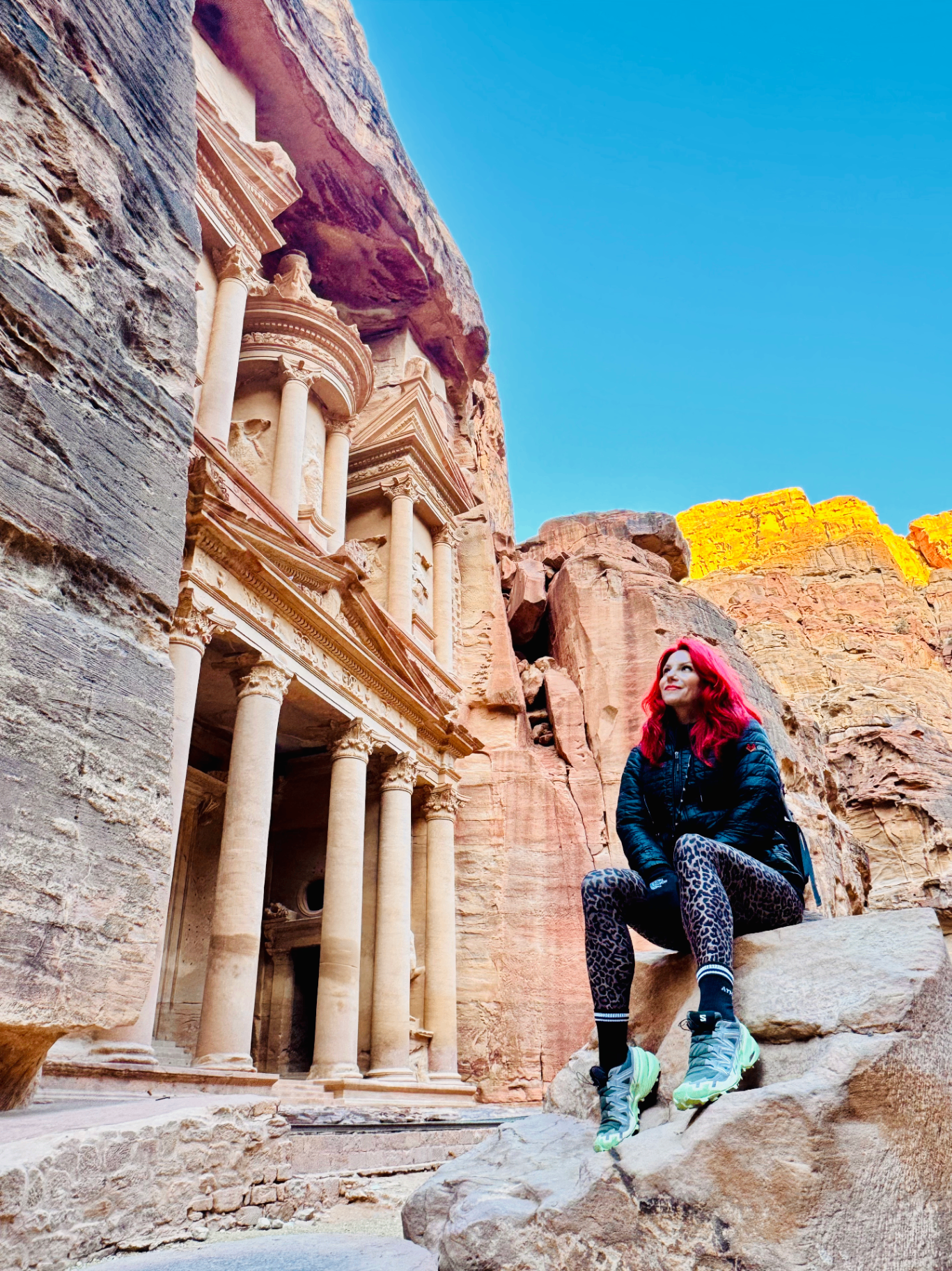 Emily Lucie sitting on a rock at the Treasury in Petra, hot pink hair, looking up at the cliffs
